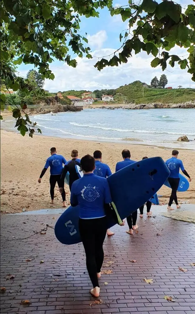 Team members in wetsuits carry surfboards down a ramp to the beach