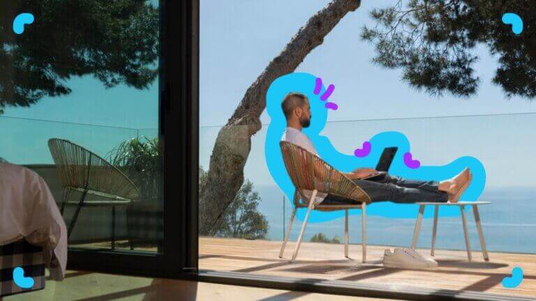 A man sitting in a chair with a laptop in front of a window, engaging remote workers.