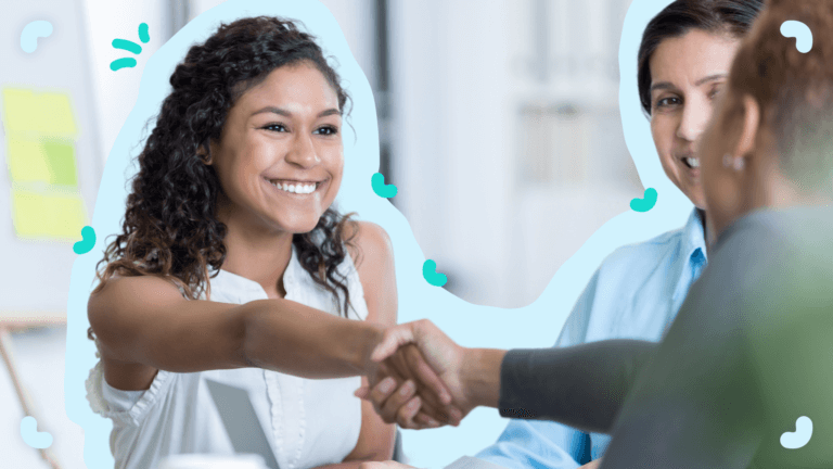 Three people sitting at a table, with one person on the left smiling and shaking hands with another person across from her. Another person sits next to her, smiling—perhaps discussing automated employee onboarding for new hires.