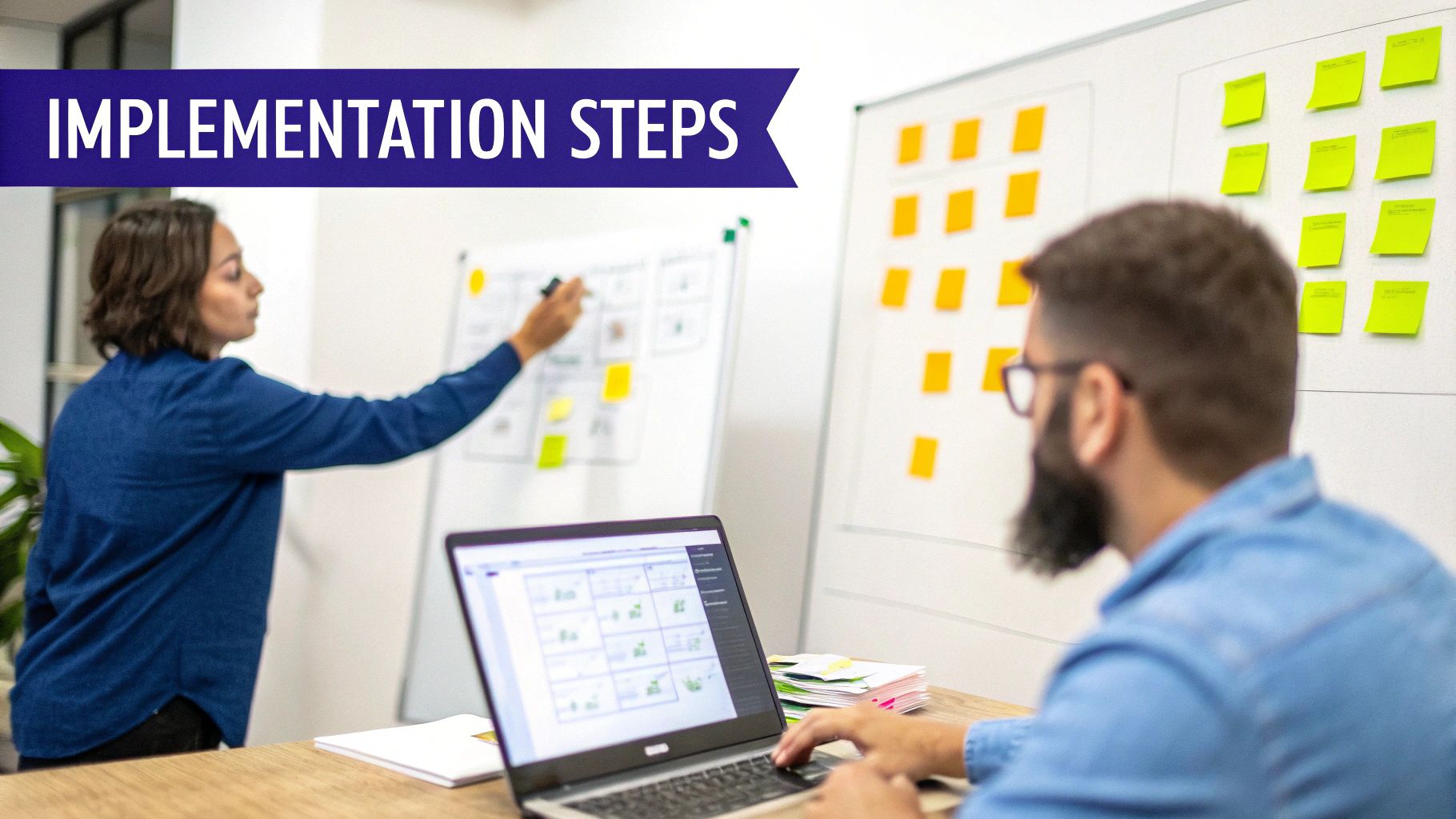 Two colleagues working on implementation steps, one writing on a whiteboard, the other using a laptop.
