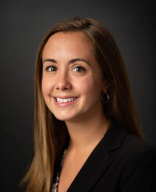 A woman in a black suit, adorned with employee training knowledge, smiles for the camera.