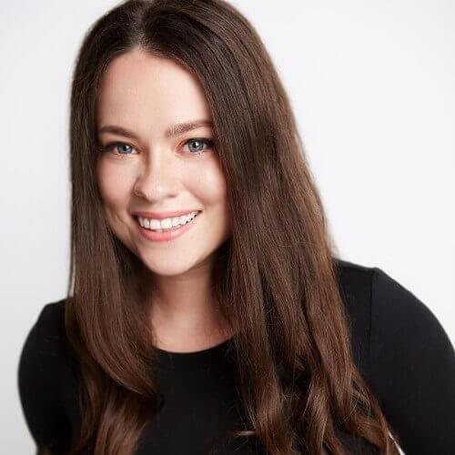 A woman with long brown hair smiling in front of a white background.