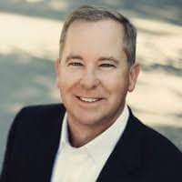 A man in a suit smiling in front of a tree during his SOP training.