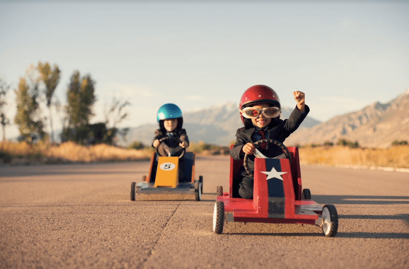 Two children following the procedures of safely riding in a toy car on a road.