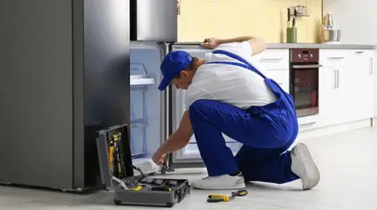 A man performing repair procedures on a kitchen refrigerator.