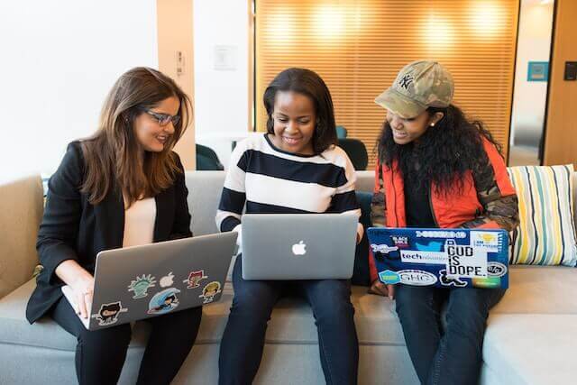 Three women building a learning culture while sitting on a couch with laptops.