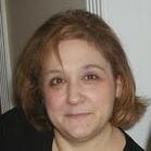 A woman with short brown hair and a neutral expression is looking at the camera. She is indoors, with a white wall and door frame in the background, possibly preparing for an onboarding session.